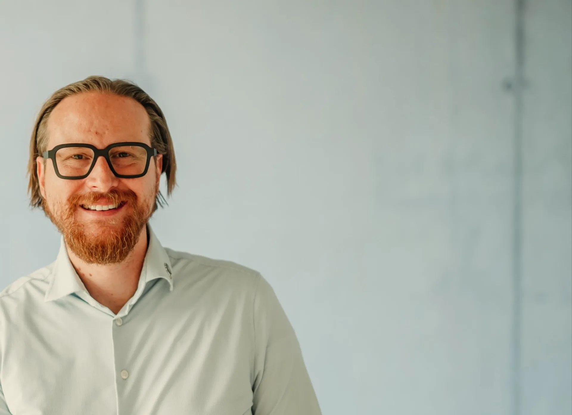 Dr. Marco Lück im hellen Hemd vor einer hellen Betonwand, er lächelt.